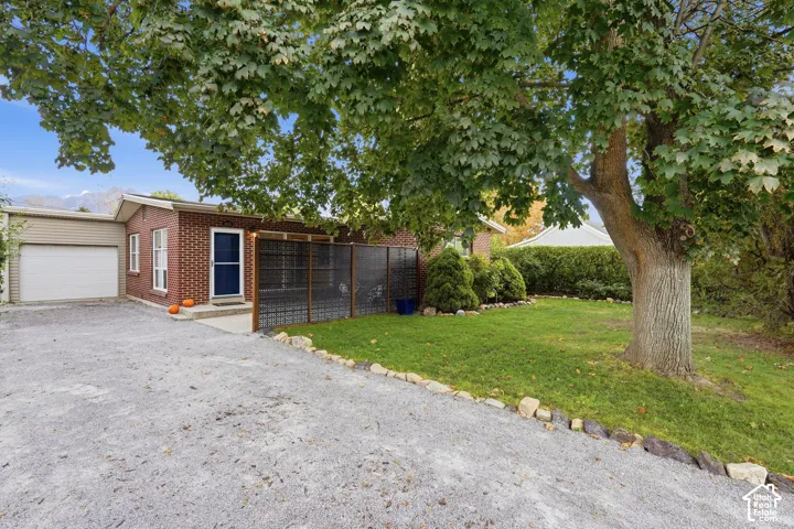Brick exterior with an attached garage, gravel driveway, and a front lawn with a mature tree