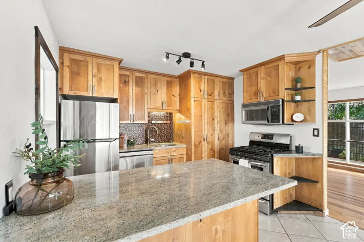 Kitchen featuring wood cabinetry, stainless steel appliances, a tiled backsplash, a kitchen island with stone countertops, and recessed lighting