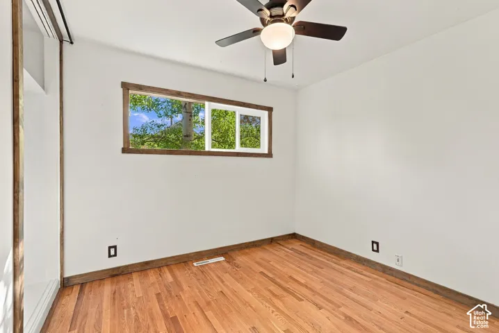 Hardwood flooring, wood-framed window, ceiling fan with integrated lighting, white walls