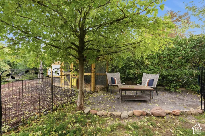 Pebble patio space featuring a low stone border, mature tree, and decorative metal fencing