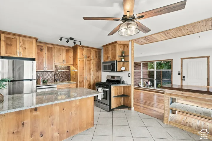 Kitchen featuring wood cabinetry, stainless steel appliances, a center island with a granite countertop, a tile backsplash, and tile flooring