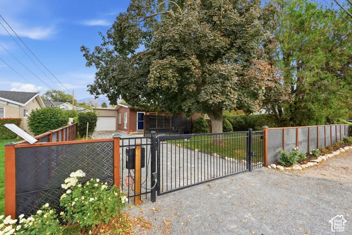 Gated driveway entrance with decorative metal panel fencing, mature trees, and a brick-front residence