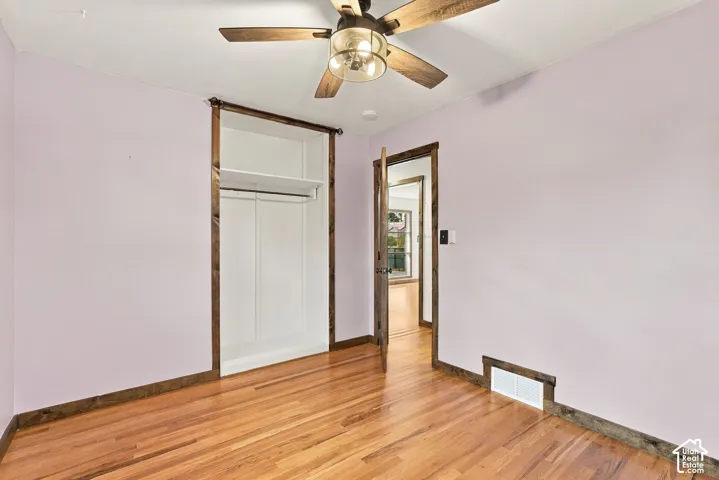 Hardwood flooring, ceiling fan with light fixture, built-in closet with shelving and hanging rod, and wood-trim doorways