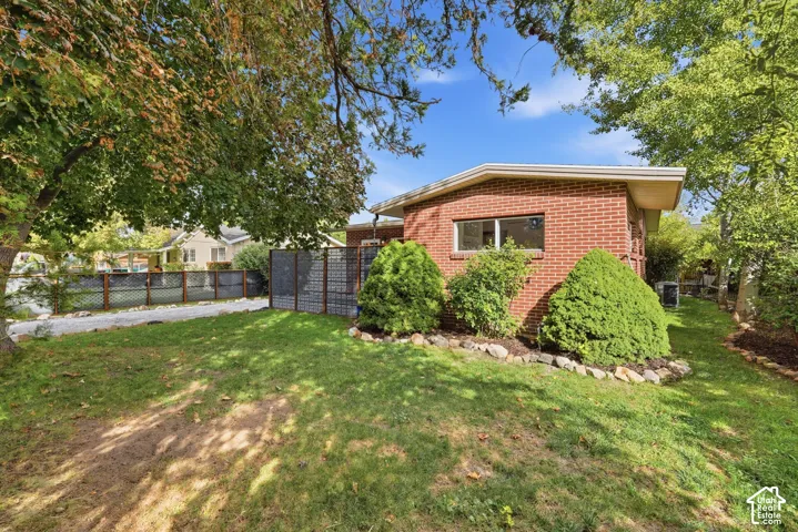 Brick exterior with multiple windows, mature landscaping, and a fenced perimeter