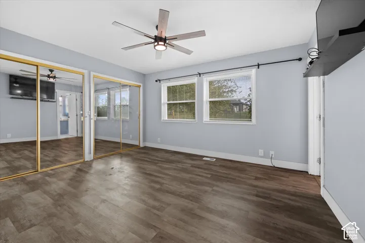 Room featuring wood-finish flooring, dual mirrored sliding-door closets, a ceiling fan with integrated lighting, and two windows