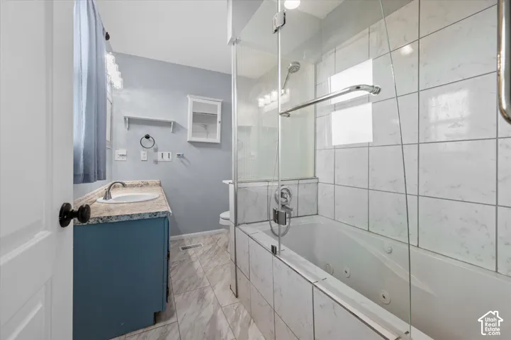 Bathroom featuring a jetted tub with a glass enclosure, tile surround, vanity with a stone-finish countertop, and tile flooring