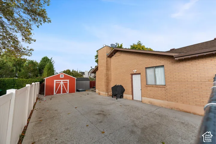 Rear exterior area featuring a concrete patio, brick siding, a detached red storage shed, and a full-height white vinyl privacy fence