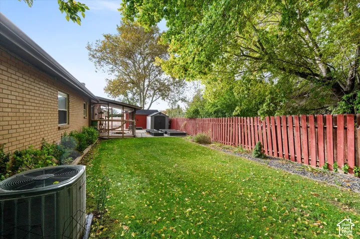 Rear exterior featuring a brick facade, covered patio, fenced yard with grass lawn, and mature canopy trees