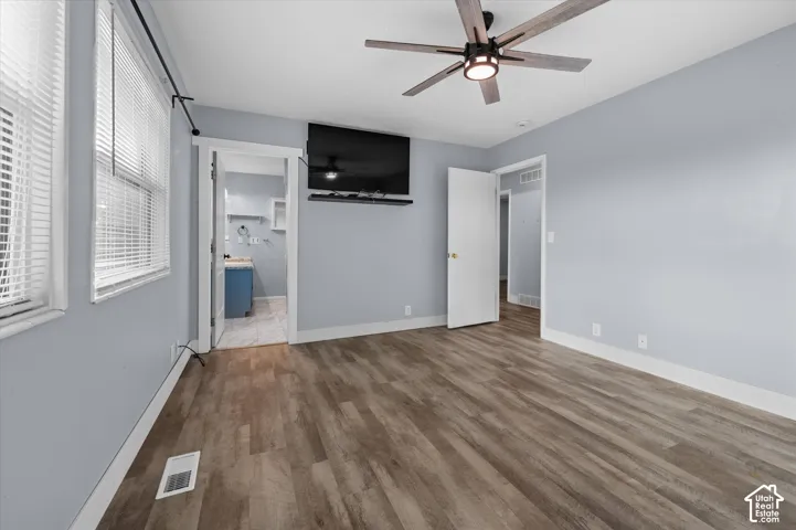 Interior room featuring wood-finish flooring, a multi-blade ceiling fan with integrated lighting, and horizontal window blinds