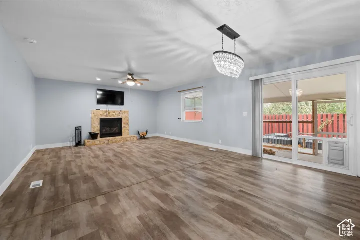 Living area featuring wood-finish flooring, a stone-surround fireplace, a ceiling fan, a crystal-style chandelier, and sliding glass doors with exterior access