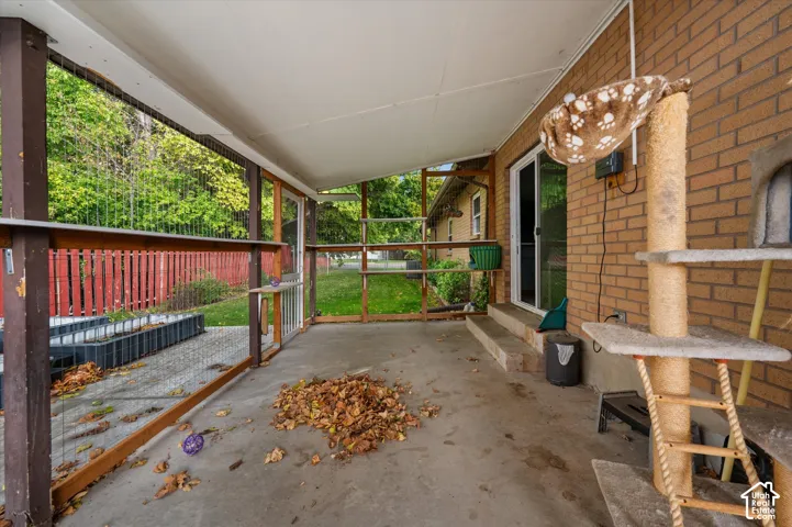 Covered patio featuring concrete flooring, brick exterior wall, and wire mesh enclosure