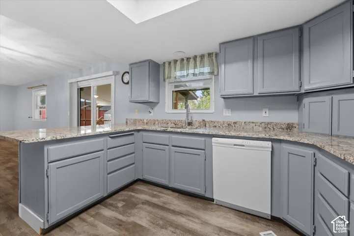 Kitchen featuring light gray cabinetry, stone-patterned countertops, wood-finish flooring, a skylight, and a stainless steel faucet