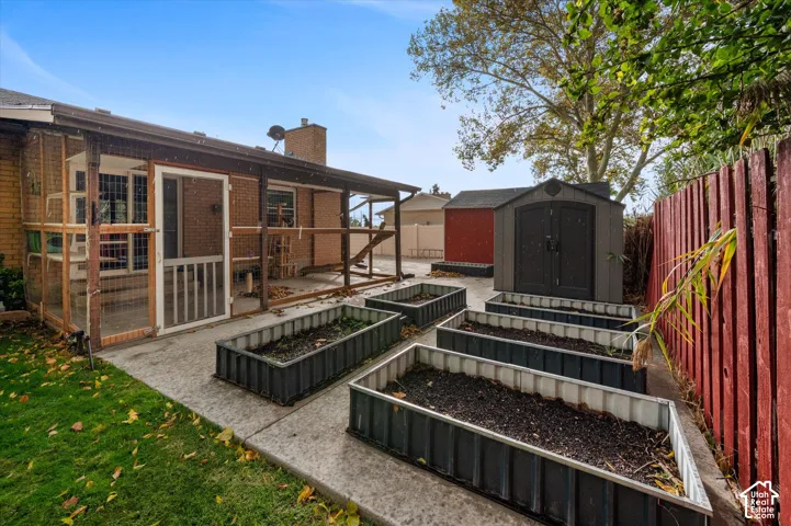 Backyard featuring a screened-in porch, multiple corrugated metal raised garden beds, a detached resin storage shed, and a privacy fence
