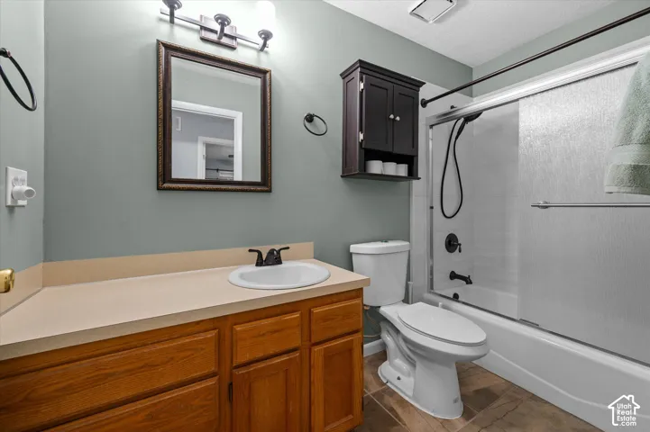 Bathroom featuring wood-finish vanity cabinetry, solid-surface countertop with integrated basin, dark-finish wall-mounted storage cabinet, and tub-shower combination with sliding glass doors