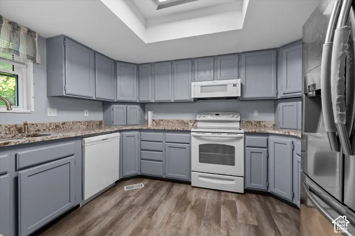 Kitchen featuring shaker-style cabinetry, stone-finish countertops, wood-finish flooring, a stainless steel refrigerator, and a skylight