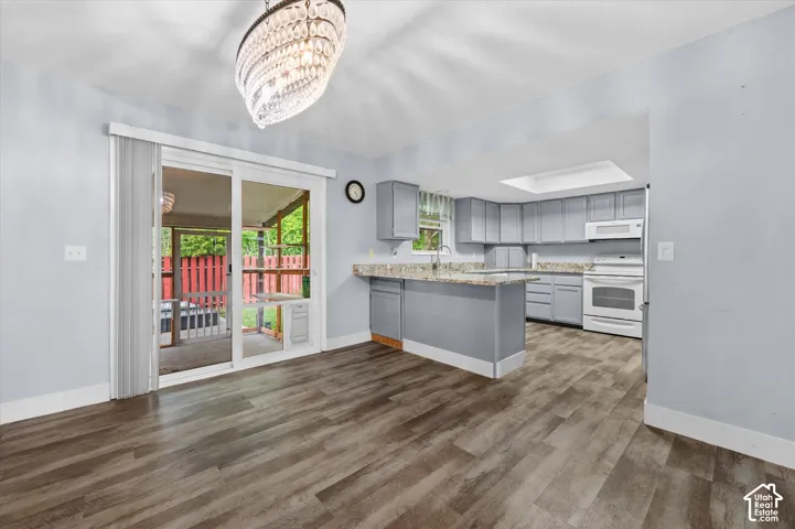 Kitchen featuring a peninsula, light-toned stone-finish countertops, wood-finish flooring, a skylight, and a crystal-style chandelier
