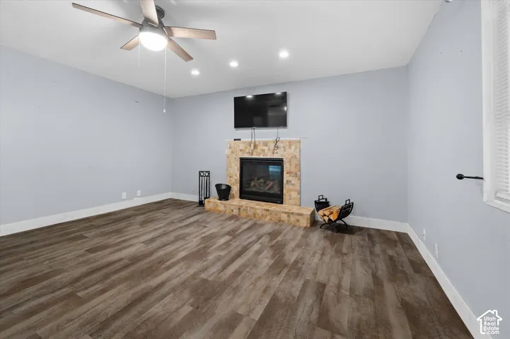 Living area featuring wood-finish flooring, a fireplace with a textured stone surround and raised hearth, recessed lighting, and a multi-blade ceiling fan