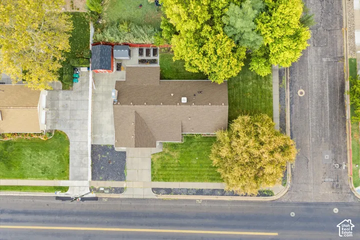 Aerial perspective featuring a multi-pitched shingled roof, concrete driveway, detached storage structure, and established landscaping