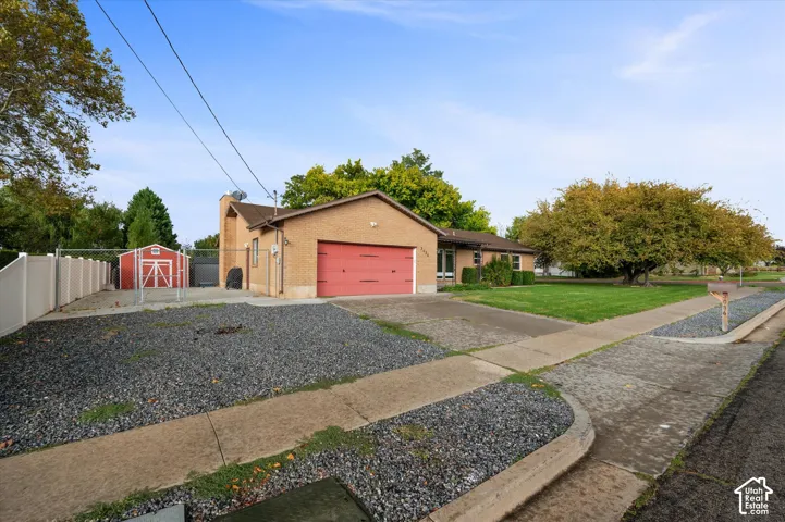 Brick exterior single-story residence featuring an attached two-car garage, gravel side parking, detached storage structure, and perimeter fencing