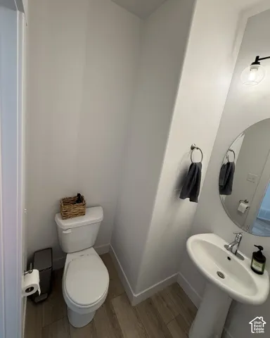 Pedestal sink with a chrome faucet, oval mirror, wood-finish flooring, and a modern light fixture