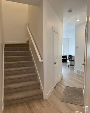 Carpeted staircase with a white handrail, wood-finish flooring, white interior doors, and recessed ceiling lighting