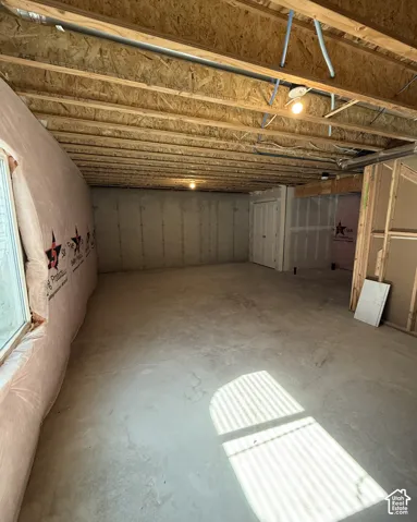 Unfinished basement with exposed ceiling joists, concrete flooring, and a window