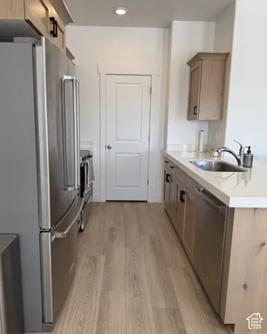 Stainless steel refrigerator, wood-finish flooring, undermount stainless steel sink, light-toned cabinetry, and solid surface countertops