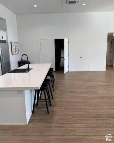 Kitchen island with a white countertop and integrated sink, stainless steel refrigerator, wood-finish flooring, and recessed lighting