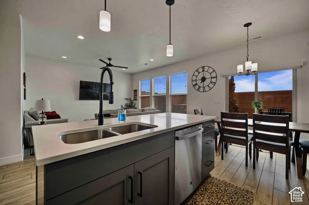 Kitchen island with a double basin sink, stainless steel dishwasher, and pendant lighting
