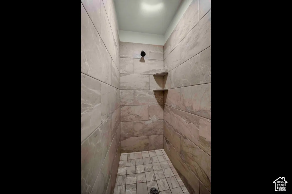 Tiled shower stall featuring a fixed shower head, two built-in corner shelves, and a tiled floor with a center drain