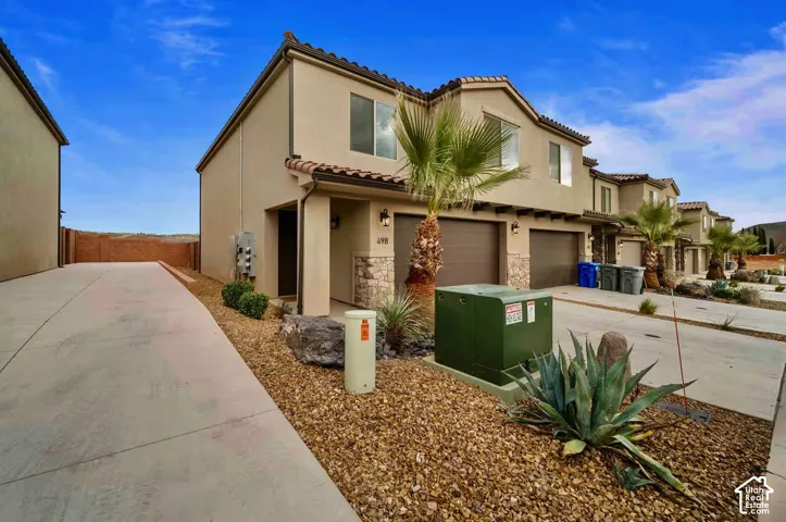Stucco exterior with stone accents, attached garage, tile roof detailing, and low-maintenance xeriscape landscaping