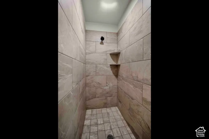Tiled shower stall featuring a fixed shower head, two built-in corner shelves, and a tiled floor with a center drain