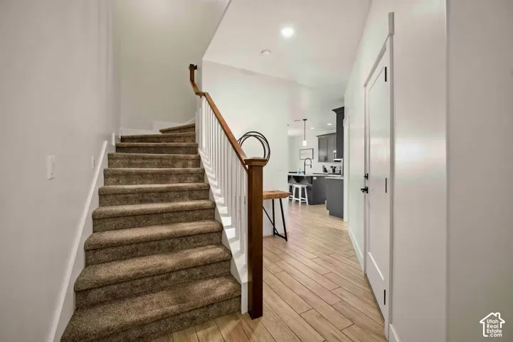 Carpeted staircase with wood handrail, white balusters, and wood-finish flooring