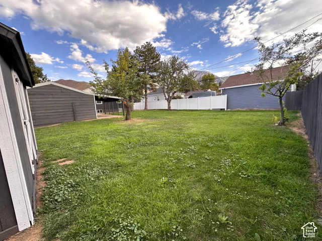 Expansive backyard featuring a lawn, mature trees, white vinyl privacy fencing, and a detached storage structure