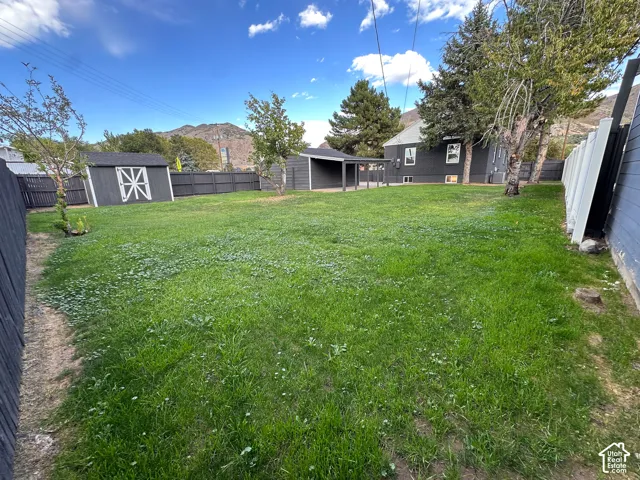Expansive backyard featuring a large grass lawn, perimeter privacy fencing, detached storage shed, covered outdoor structure, and mountain backdrop