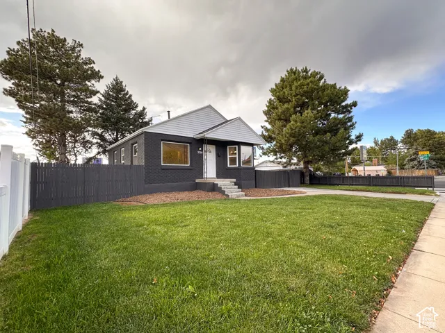 Exterior featuring a painted brick facade, gabled roofline, front lawn, and perimeter privacy fencing