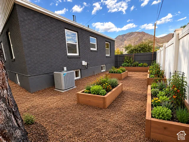 Painted brick exterior with multiple raised garden beds, crushed stone landscaping, privacy fencing, and mountain backdrop