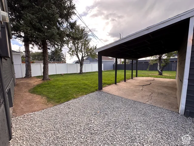 Covered carport featuring a concrete pad, gravel parking area, grass lawn, and perimeter privacy fencing