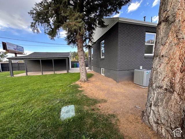 Exterior featuring dark-toned masonry siding, a detached covered carport, a fenced yard, and mature pine trees
