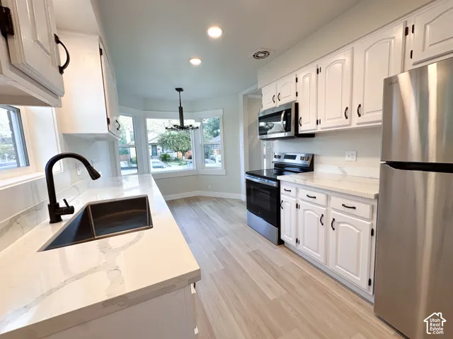 Kitchen featuring white cabinetry, stone-look countertops, stainless steel appliances, a matte black faucet, and wood-finish flooring