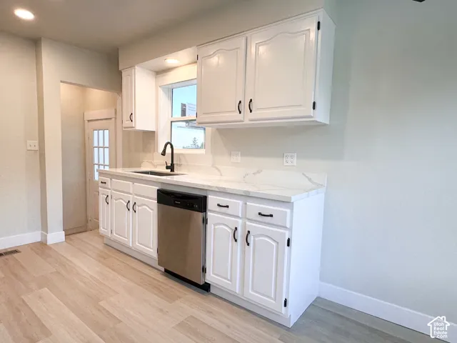 Kitchen featuring white cabinetry, light-toned stone-finish countertops, matte black hardware, integrated stainless steel dishwasher, and wood-finish flooring