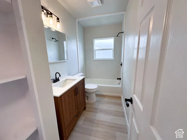 Bathroom featuring a vanity with a white countertop, wood-finish cabinetry, matte black fixtures, and wood-finish flooring