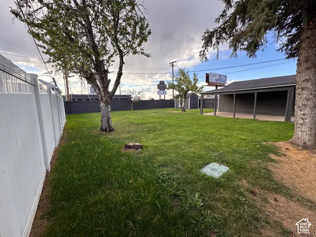 Backyard featuring a covered patio, vinyl fencing, mature trees, and a detached storage structure