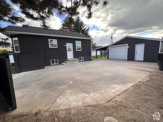 Detached garage with a white garage door, concrete driveway, dark-painted exterior, white entry door, and concrete steps