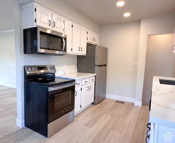 Kitchen featuring white shaker-style cabinetry, stainless steel appliances, light-toned stone-finish countertops, and wood-finish flooring
