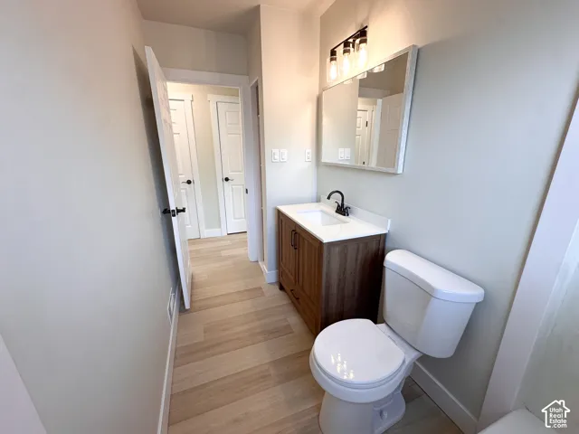 Bathroom featuring a vanity with a white countertop and rectangular sink, wood-finish cabinet, matte black faucet, three-light fixture, and wood-finish flooring