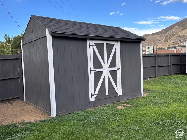 Exterior storage shed featuring a dark wood-composite siding, contrasting white trim, gable roof with asphalt shingles, and a barn-style door with metal hardware