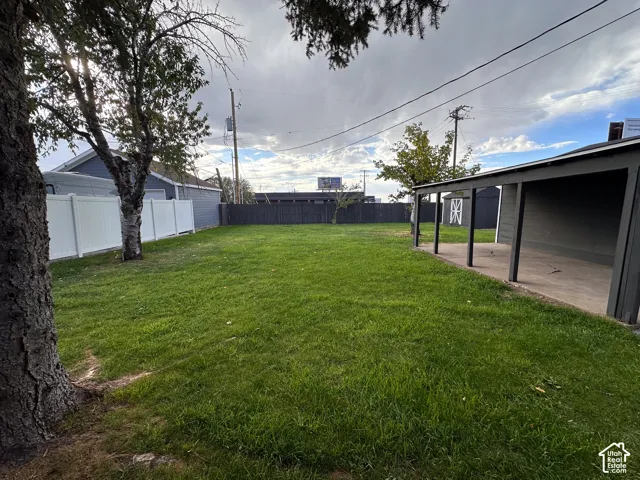 Expansive backyard featuring a covered patio, vinyl perimeter fencing, mature trees, and a detached storage structure