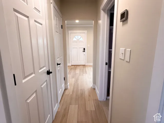 Hallway featuring wood-finish flooring, six-panel interior doors with matte black hardware, and an exterior door with a decorative arched window inlay