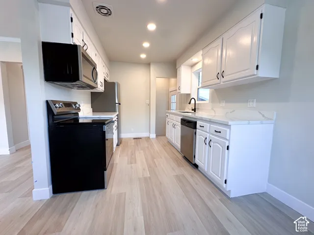 White cabinetry with black hardware, wood-finish flooring, recessed lighting, and stainless steel appliances